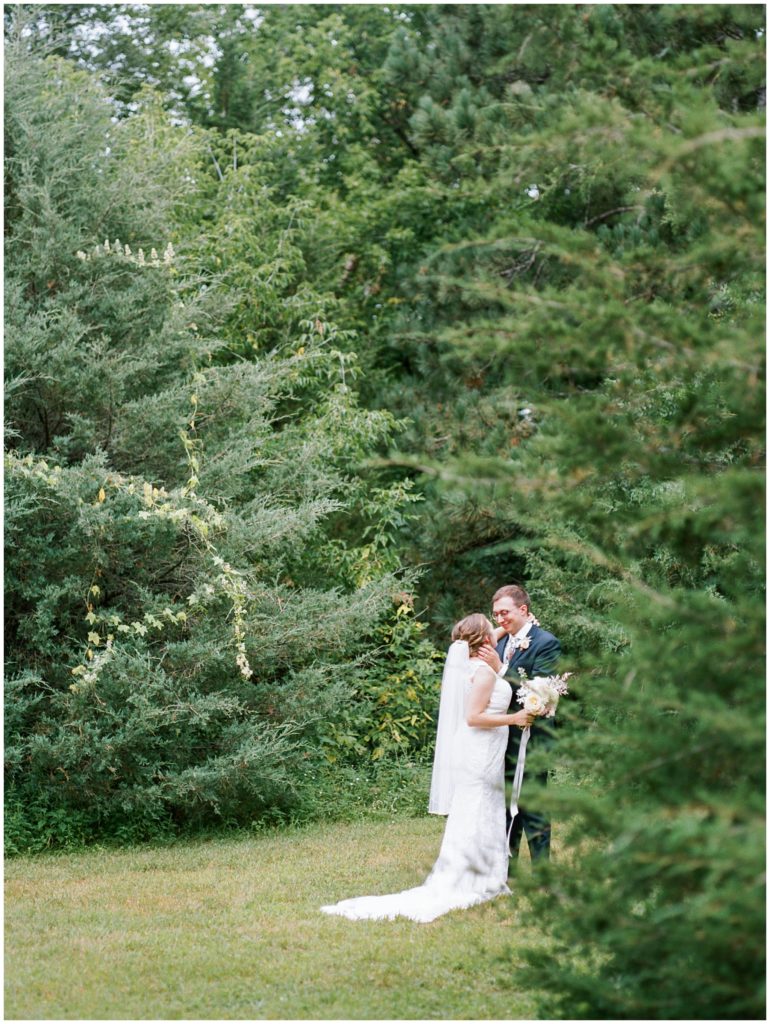 Fine art portrait of newly married couple surrounded by greenery and trees outside in the distance