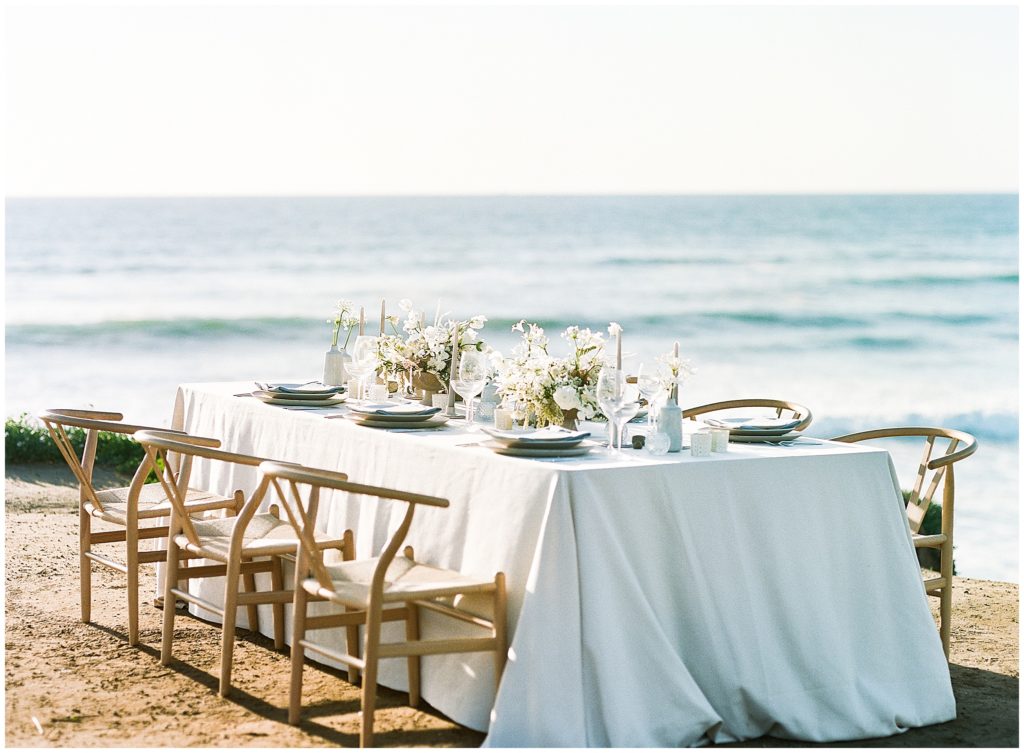 A head reception table on the beach, designed by Casa de Perrin, featuring BBJ Linen white tablecloth, and Max Owens Design flowers
