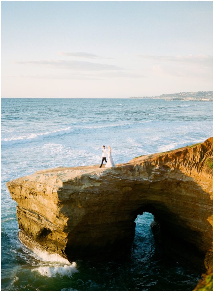 A gorgeous landscape photo of a couple in the distance on a cliff overlooking the Pacific Ocean, walking hand in hand at sunset on the ocean