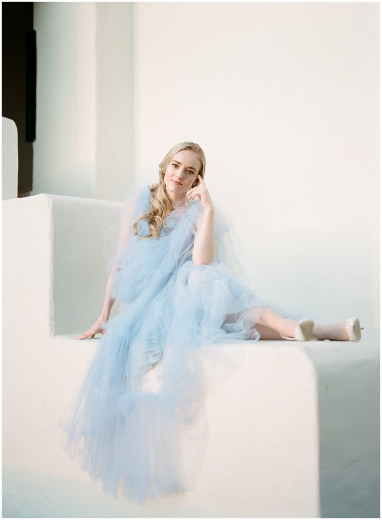 A bride sits outside on white steps in a blue wedding gown, smiling on the day of her San Diego destination wedding
