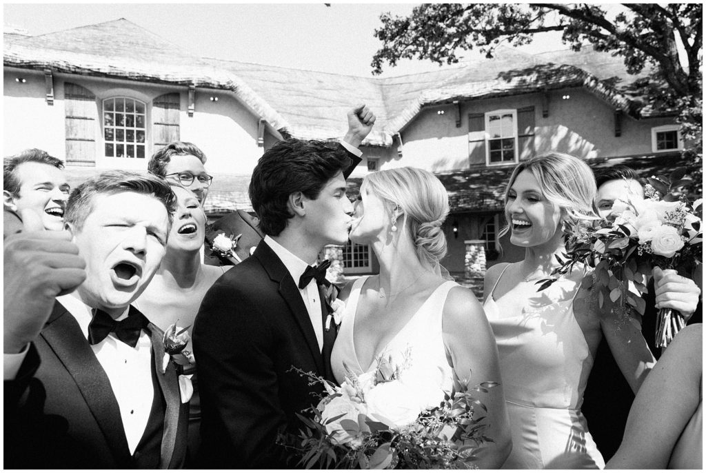 Goofy photo of couple kissing and wedding party cheering
