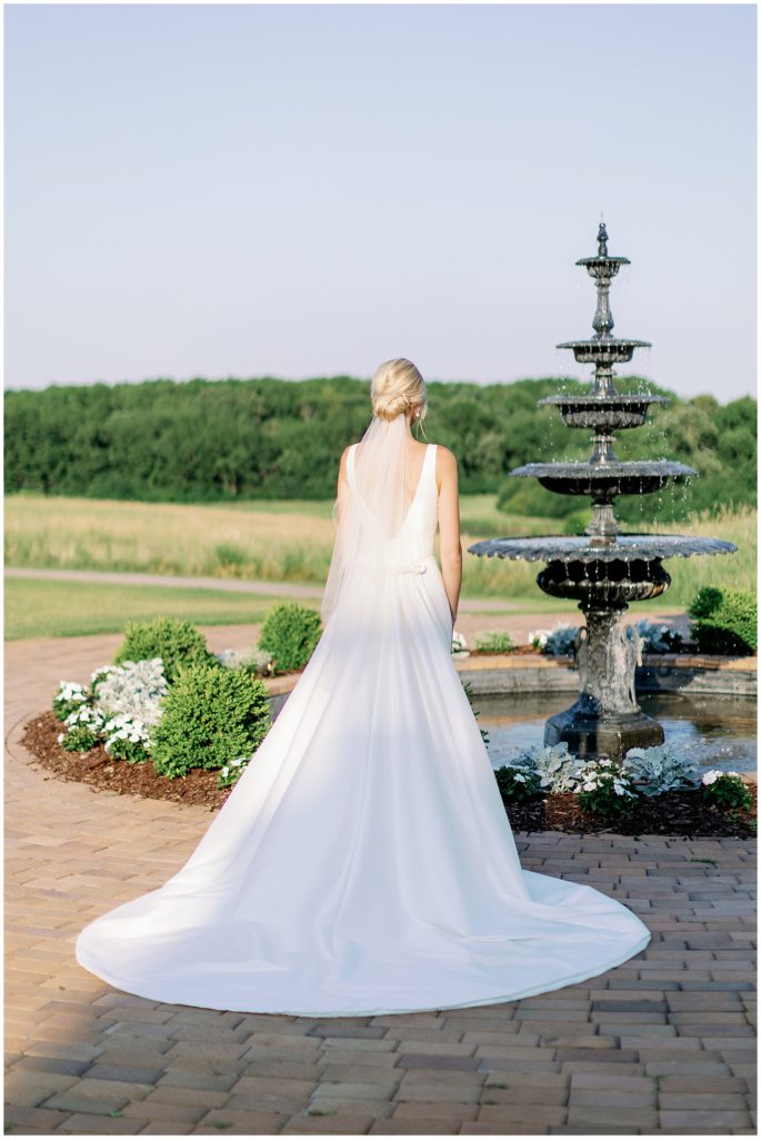 Bride standing in front of classic estate fountain in Minnesota