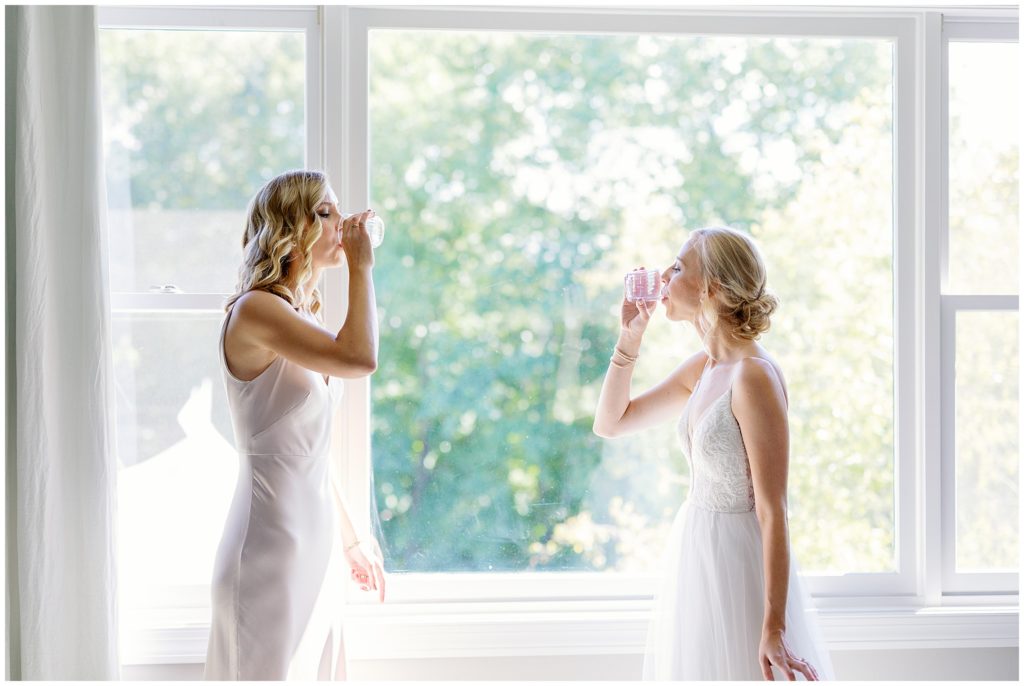 Bride and sister take a shot in front of green window in Minnesota wedding